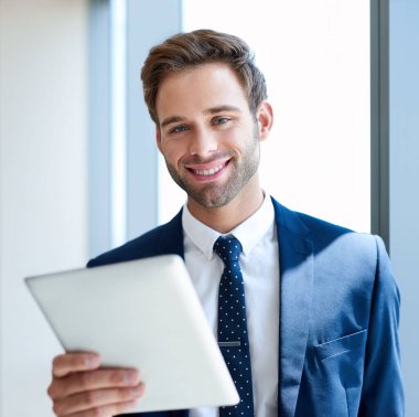 Ofisinde dijital tablet tutan genç bir işadamının portresi ve dostça bir ifadeyle kameraya gülümsüyor.