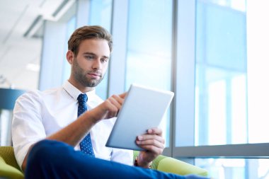 Genç ve yakışıklı bir girişimcinin geniş pencereli modern ofis alanında dijital tablet kullanmasının düşük açılı görüntüsü.
