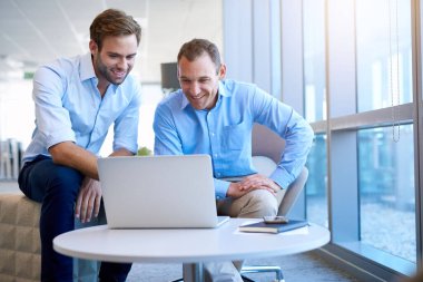 Genç işadamı, büyük pencereli, parlak, modern bir ofiste, bir iş arkadaşıyla bilgisayarında iyi haberler paylaşıyor.