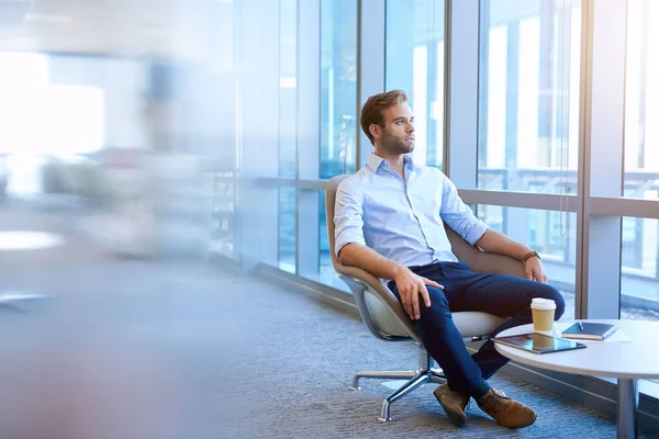 Handsome young business entrepreneur sitting in a modern office space, Looking out of large windows and thinking optimistically about the future