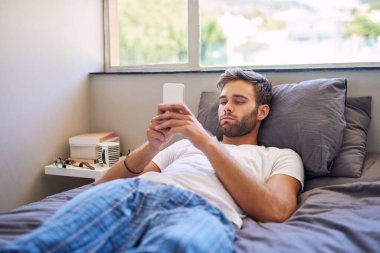 Sabahları yatakta yatarken cep telefonu kullanan pijamalı yakışıklı bir genç.