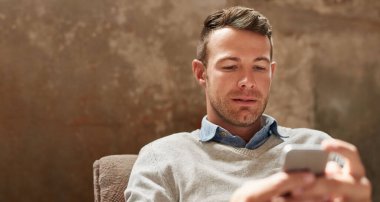 Modern bir ofiste otururken sıradan giyinmiş genç bir işadamı cep telefonundan mesaj okuyor.