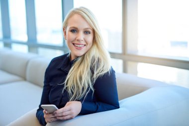 Modern bir ofiste pencerenin önünde oturan gülümseyen genç bir iş kadınının portresi cep telefonuyla mesaj gönderiyor. 