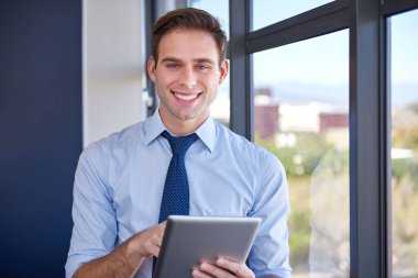 Ofisinde büyük pencerelerin yanında dijital tablet tutan genç bir işadamının portresi, kameraya güvenle gülümsüyor.