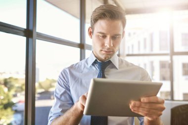 Ofisinde duran yakışıklı genç işadamı büyük pencerelerden içeri giren, elinde dijital bir tablet tutan ve dokunmatik ekranı kullanan...