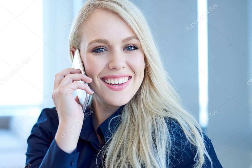 Portrait of a smiling young businesswoman having a conversation on her cellphone while sitting in a modern office 