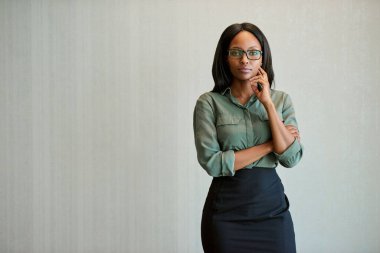 Modern bir ofiste odaklanmış, gözlüklü ve eli çenesinde duran genç bir iş kadınının portresi.