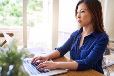 Genç Asyalı girişimci evinde, oturma odasında tek başına oturmuş bir dizüstü bilgisayarla çalışıyor. 