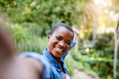 Gülümseyen Afro-Amerikan kadın yazın parkta eğlenirken selfie çekiyor.
