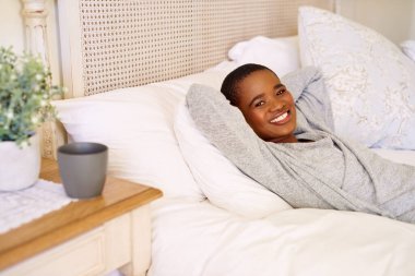 Sabahları elleri başının arkasında yatarken gülümseyen Afro-Amerikan bir kadının portresi.
