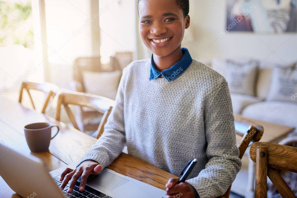 Portrait of a smiling young African American female entrepreneur sitting at her table at home working on a laptop  