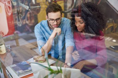 Çeşitli genç çiftler bir kafenin penceresinde otururken birlikte gülümsüyor ve dizüstü bilgisayar kullanıyorlar.