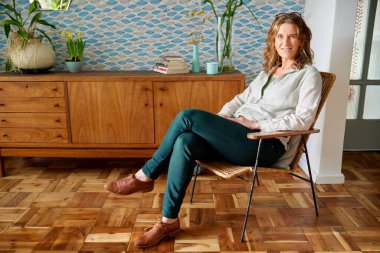 Şık dairesinde bir sandalyede otururken gülümseyen olgun bir kadının portresi.