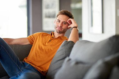 Oturma odasındaki kanepede tek başına oturmuş gülümseyen genç bir adamın portresi.