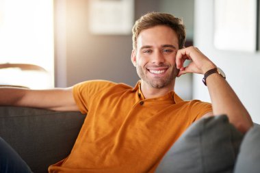 Evdeki kanepede tek başına dinlenirken gülümseyen genç bir adamın portresi.