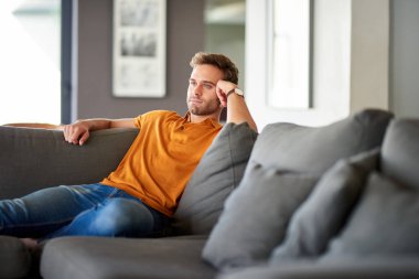 Oturma odasındaki kanepede tek başına oturan genç adam derin düşüncelere dalmış.  