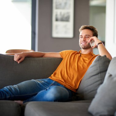 Gülümseyen genç adam evdeki kanepede tek başına dinlenirken bir arkadaşıyla cep telefonuyla konuşuyor.