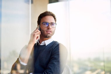 Genç işadamı, ofisinin penceresinden dışarı bakarken bir müşterisiyle konuşuyor.  