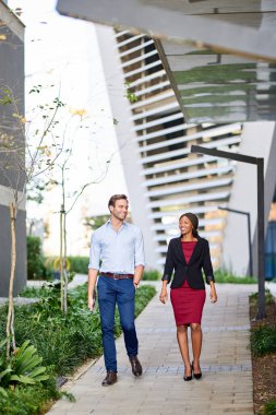 İki farklı genç iş arkadaşı ofis komplekslerinde birlikte yürüyüp sohbet ediyorlar.