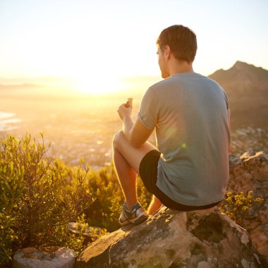 Dikiz aynasından genç bir adamın güneşin doğuşunu izlerken bir protein çubuğu yemek için duraklarken görüntüsü.