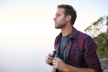 Yakışıklı genç bir erkek öğrenci, elinde dürbünle ufka bakıyor. Doğada.