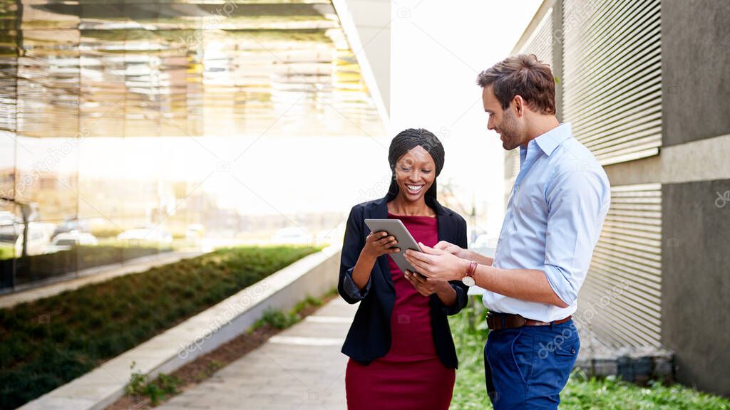 Young businesswoman standing with a male colleague outside of an office building working on a digital tablet