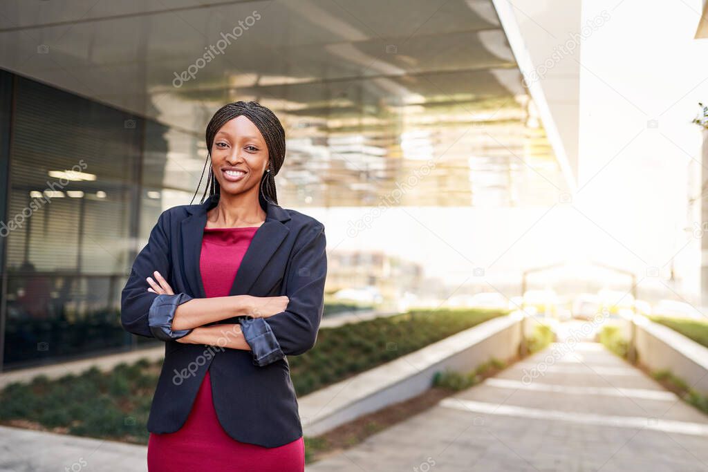 Portrait of a smiling young African American businesswoman standing with her arms crossed outside of an office building