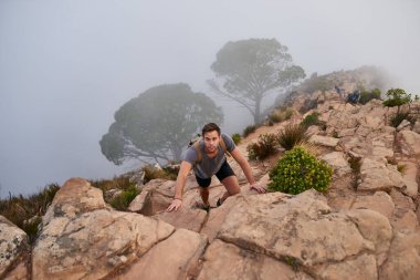 Genç bir adamın yüksek açılı manzarası dikkatle dağdaki doğa yolunda kayalara tırmanıyor.
