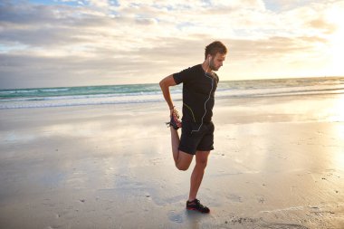 Kumsalda sabah koşusundan önce genç bir adam ayaklarını ısıtıyor.