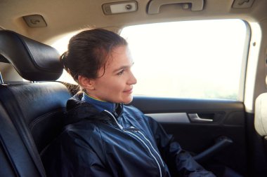 Egzersiz kıyafetli genç bir kadın arabanın arka koltuğunda sessizce oturuyor.