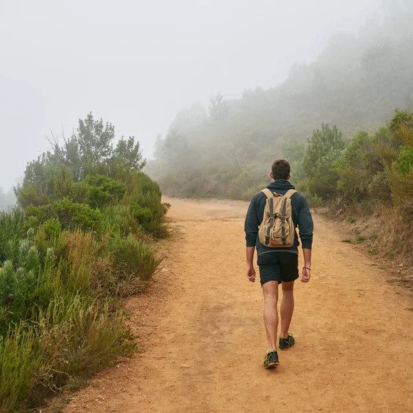 Rearview of a young man walking away from the camera on a dirt path nature trail with the natural surrounds disappearing into morning mist