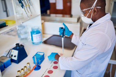 Koruyucu bir maske takan Afrikalı erkek teknisyen ve gözlük takan bir pipetle tur örnekleri hazırlıyor.
