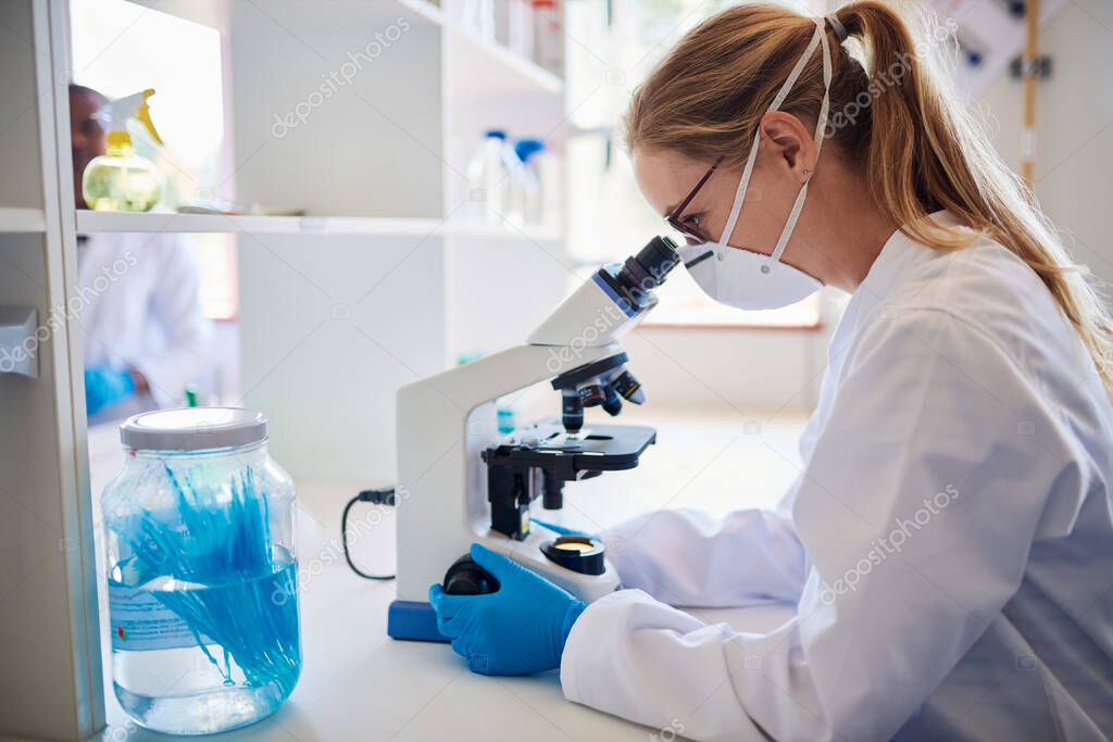 Female lab technician looking at samples through a microscope while working at a table in a lab