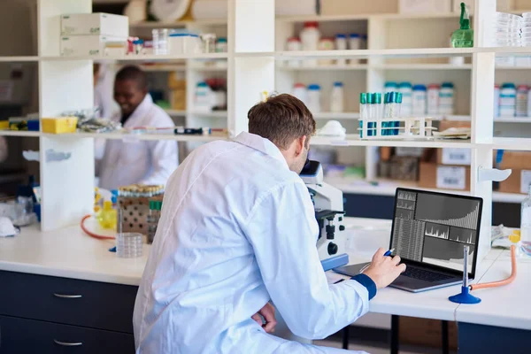 Férfi Technikus Átnéz Egy Mikroszkópon Adatokat Meg Egy Laptopban Miközben Stock Fotó