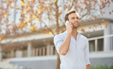 Sonbaharda modern bir ofis binasının önünde cep telefonuyla konuşan genç bir işadamı.