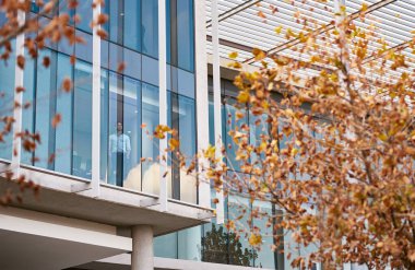 Genç işadamı pencereden dışarı bakıyor ve modern bir ofis binasının içinde dururken düşünüyor.