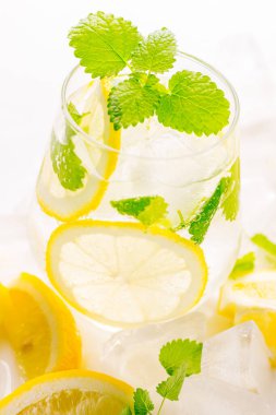 Limonata bardakta içilir: su, buz, limon dilimi ve beyaz arka planda nane.