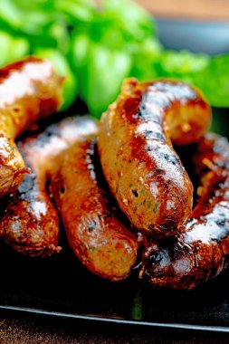 Siyah tabakta domuz eti sosisi, taze fesleğenle servis ediliyor, yakın plan.