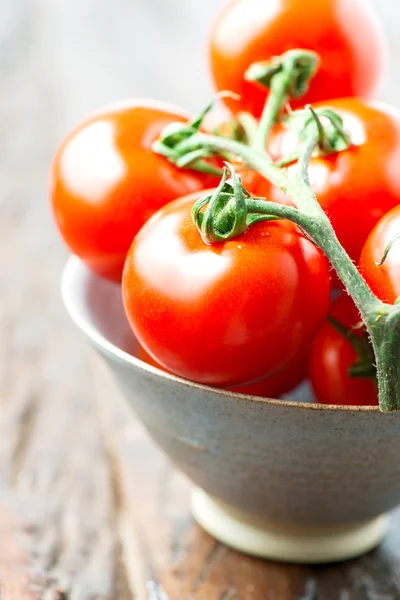 Tomatoes in a bowl on old wooden table — Stock Photo, Image