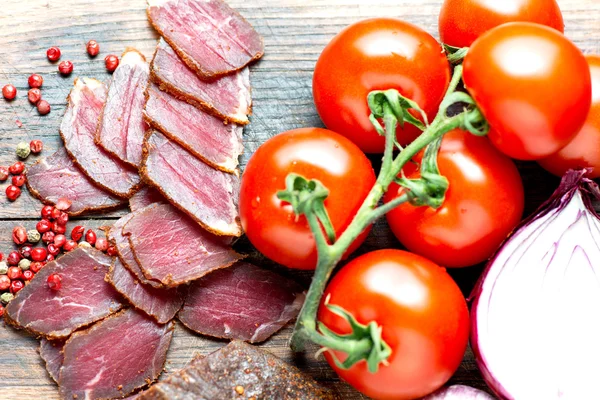 Vlees en tomaten op houten tafel — Stockfoto