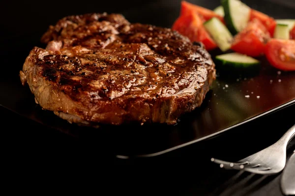 Filete a la parrilla y verduras en plato negro con tenedor — Foto de Stock