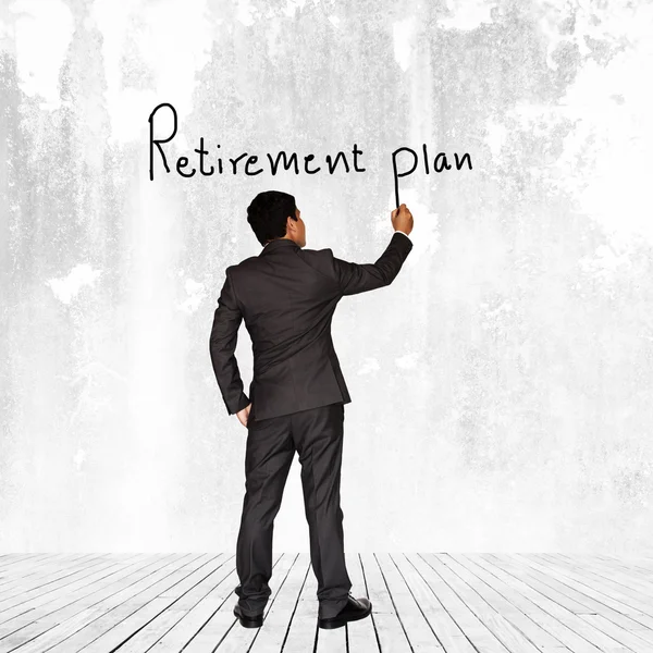 Asian businessman writing Retirement plan text on wall background — Stock Photo, Image