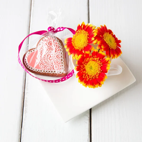 Copo cheio de flores de gerbera rosa e biscoito em forma de coração no whi — Fotografia de Stock