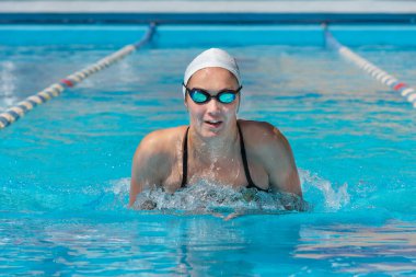 Mavi su havuzunda yüzen mayolu bir kadın.