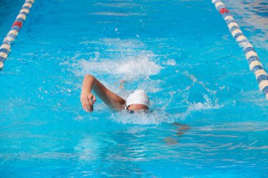 Mavi su havuzunda yüzen mayolu bir kadın.