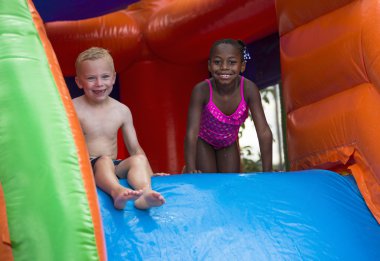 Happy kids sliding down an inflatable bounce house. clipart