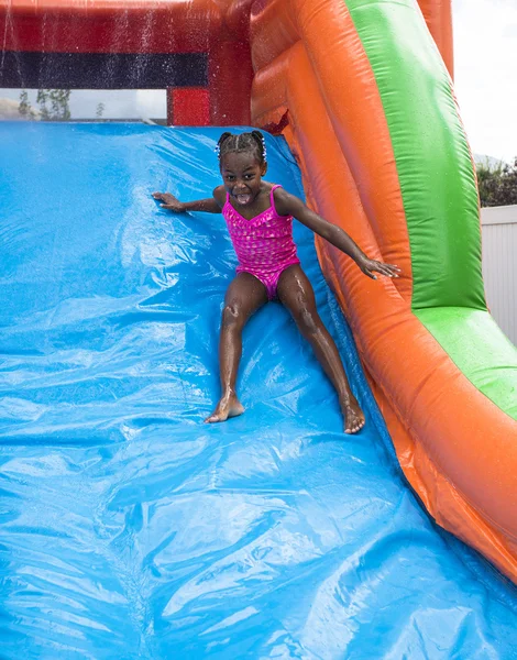 Sonriente niña jugando en una casa inflable de la despedida de la diapositiva al aire libre . —  Fotos de Stock