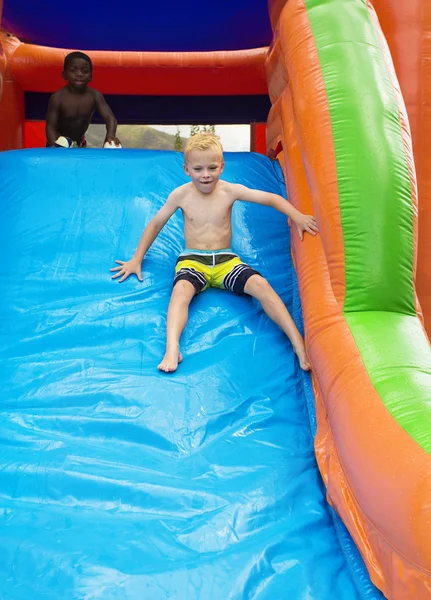 Crianças felizes deslizando para baixo uma casa inflável do salto . — Fotografia de Stock