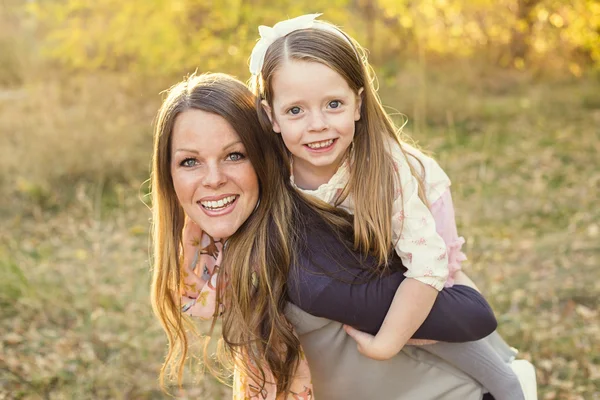 Young mother carrying her cute daughter piggyback — Stock Photo, Image