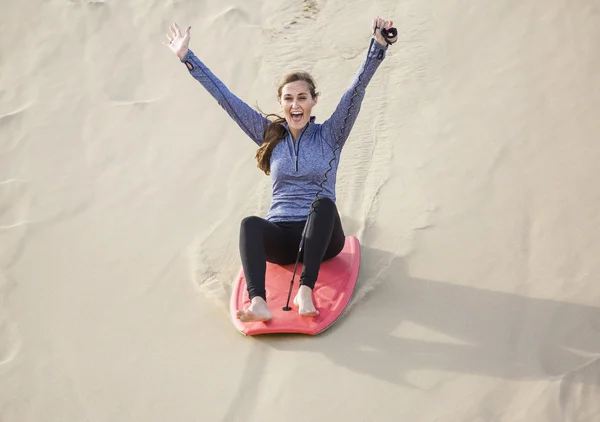 Woman riding a board down a sand dune — Stock Photo, Image